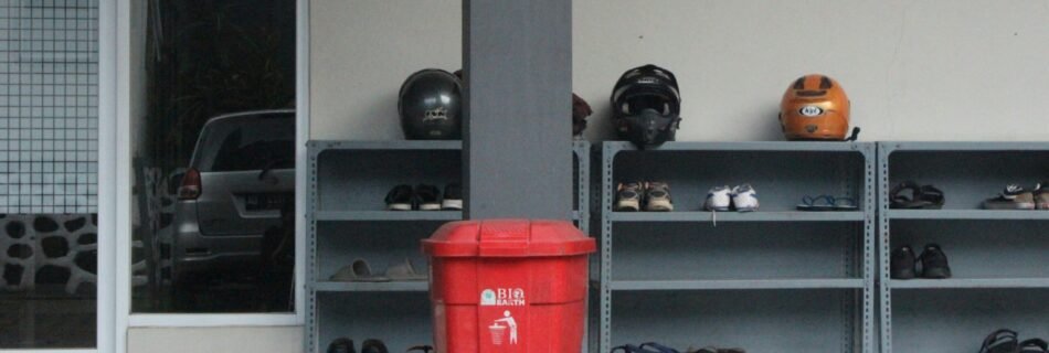 a red garbage can next to a shelf with objects on it